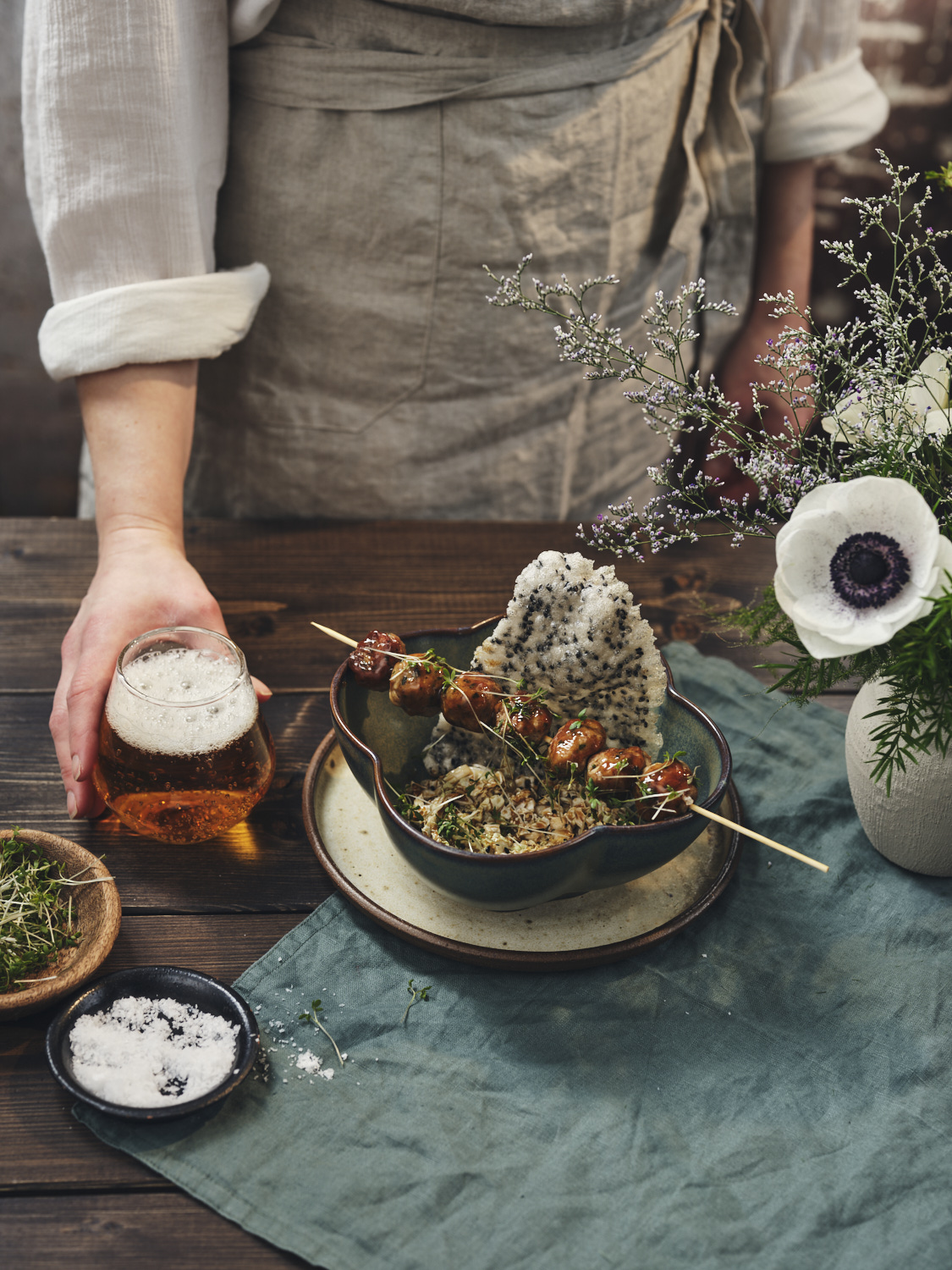 Servitören serverar ett glas öl till den japanska rätten "Niku Dango" som ligger på träbordet som är dekorerat med blommor 